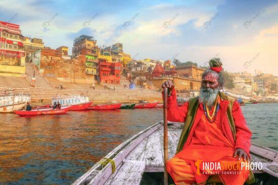 Sadhu Baba on a boat on river Ganges with Varanasi ancient city architecture at sunset