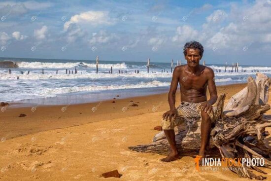 Rural Indian fisherman sitting on a tree trunk by the sea beach