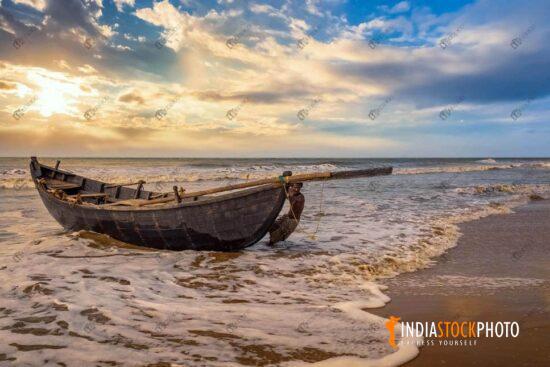 Indian fisherman tows his boat to sea shore at sunset