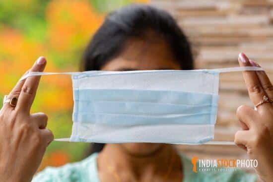 Indian woman holds a surgical face mask before wearing