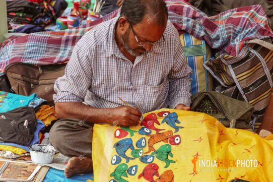 Male artist doing fabric painting on a woman saree