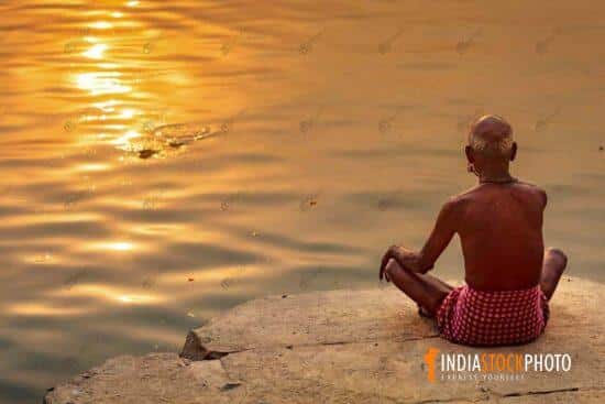 Man meditating at Ganges river bank at sunrise at Varanasi
