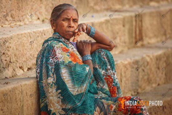 Old Indian woman sitting on the steps of Ganges Ghat at Varanasi