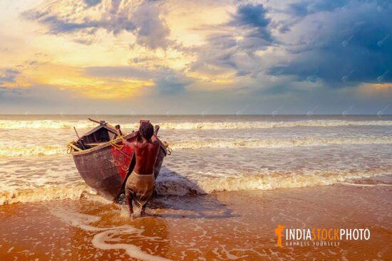 Fisherman tows his fishing boat to sea shore at sunset