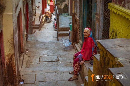 Old woman sitting at a Varanasi city alleyway with old buildings
