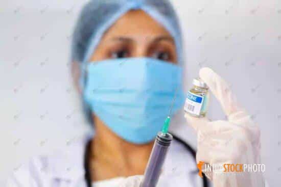 Indian lady doctor holding a syringe and vaccine bottle