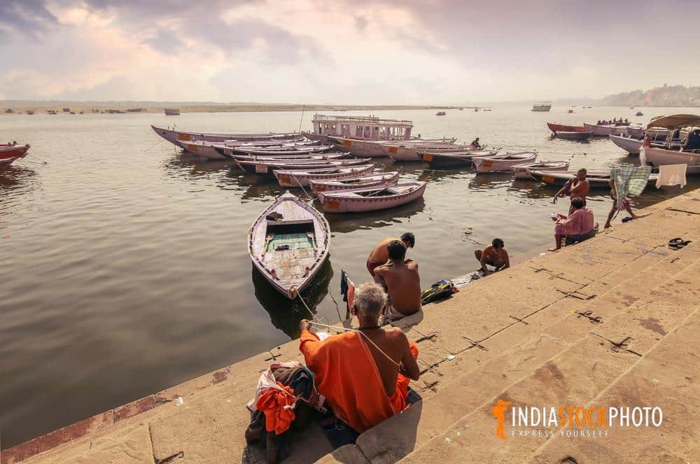 Hindu monk at the Ganges river bank with wooden boats at sunrise